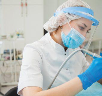 A female dentist performs a surgery dressed in full PPE