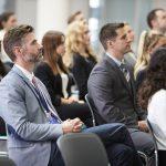 A diverse group of people watch an unseen speaker at a seminar