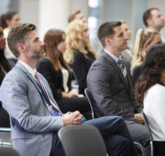 A diverse group of people watch an unseen speaker at a seminar