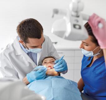 A dentist performs a routine checkup on a child, as a nurse looks on.